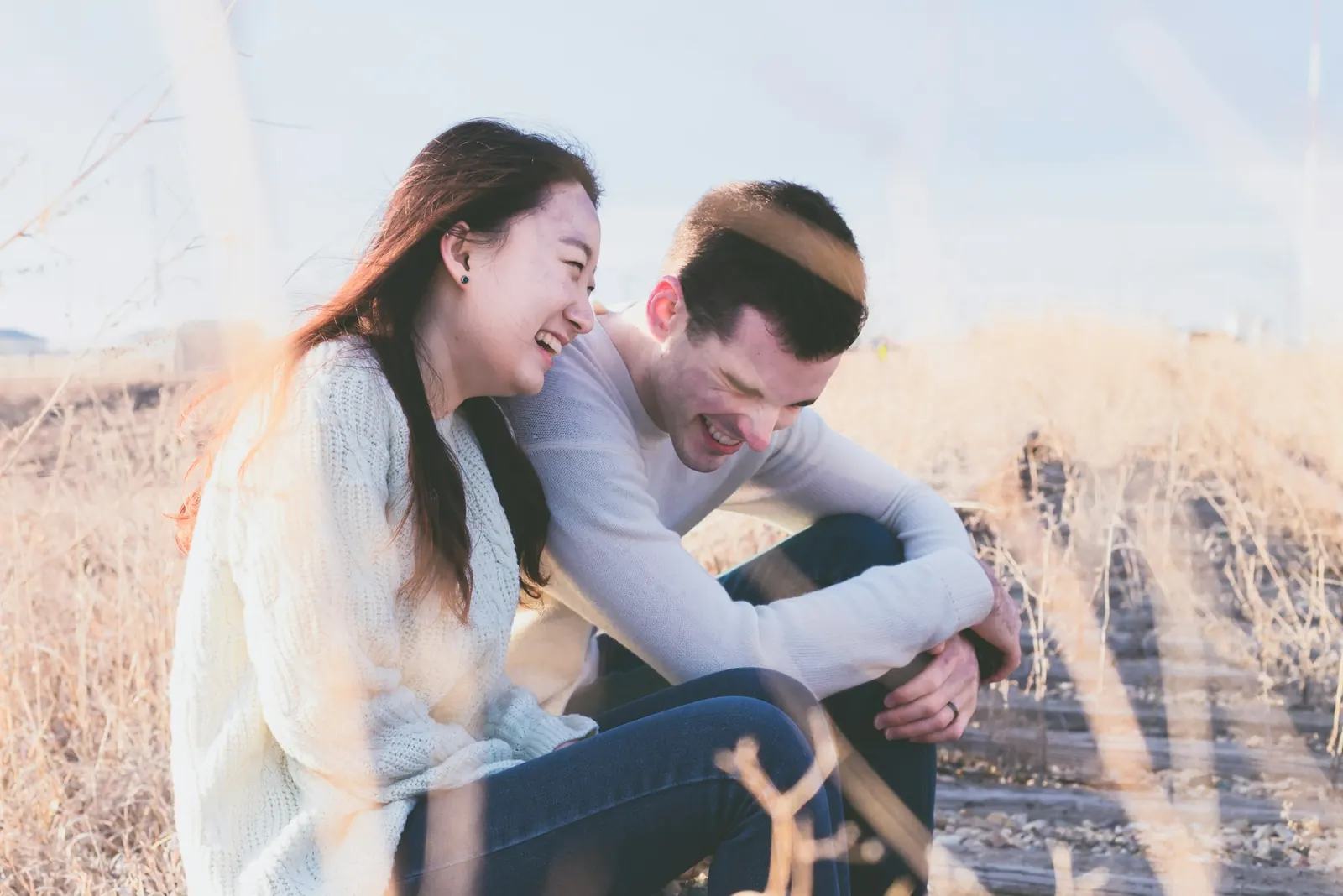A couple laughing together in a field of dry grass