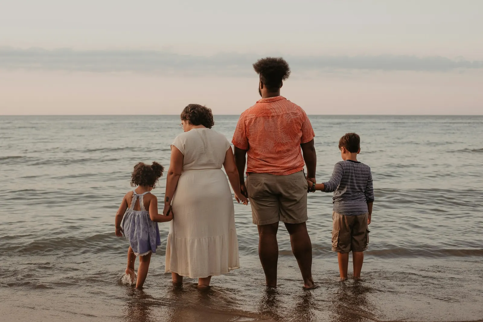 A family standing together at the water's edge, looking out to sea