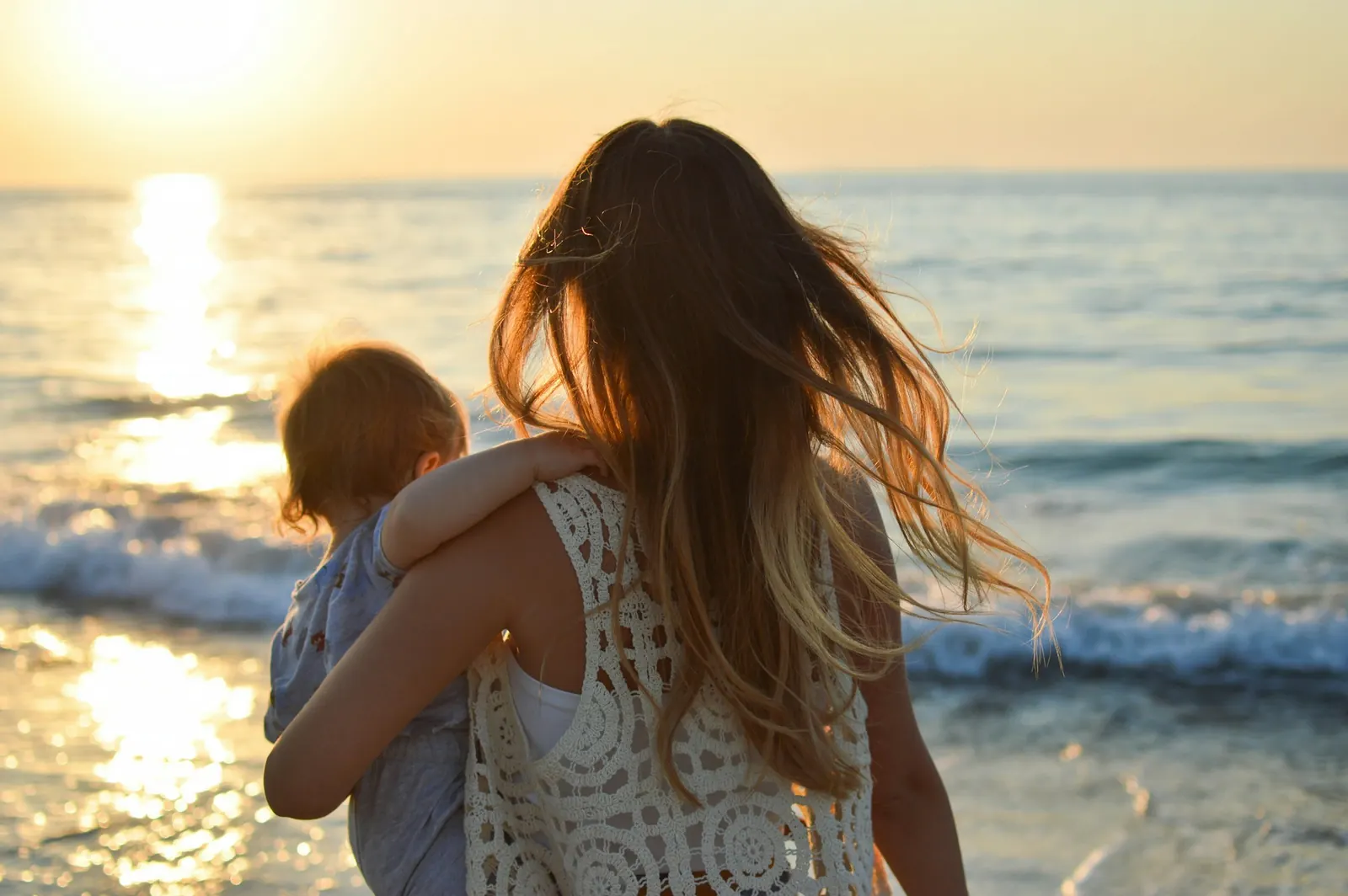 A mother carrying her young child along the shore at sunset